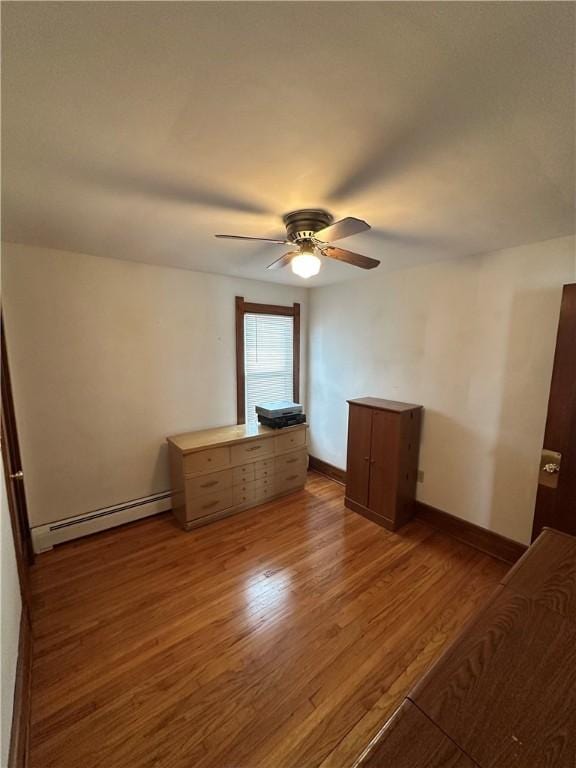 unfurnished bedroom with a baseboard heating unit, wood finished floors, a ceiling fan, and baseboards