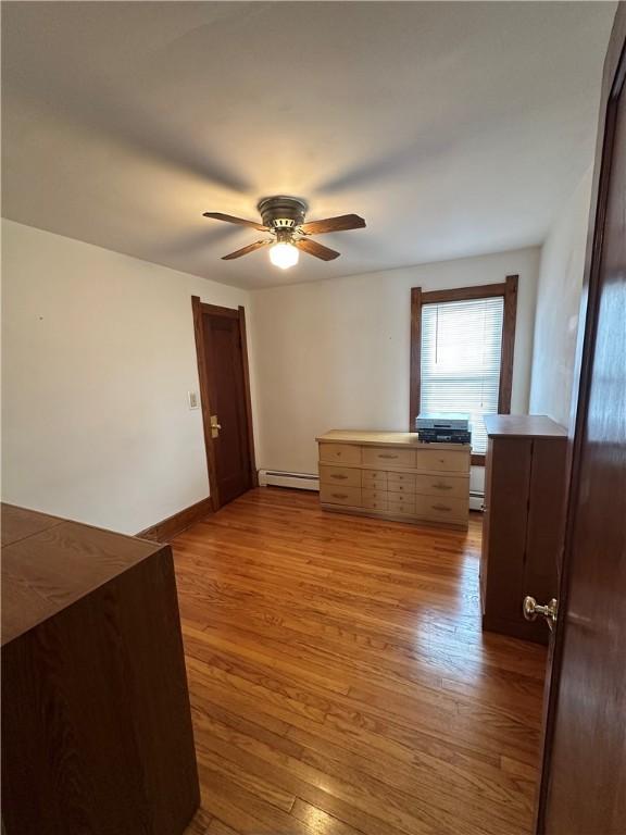 empty room with baseboard heating, light wood finished floors, a ceiling fan, baseboards, and a baseboard heating unit
