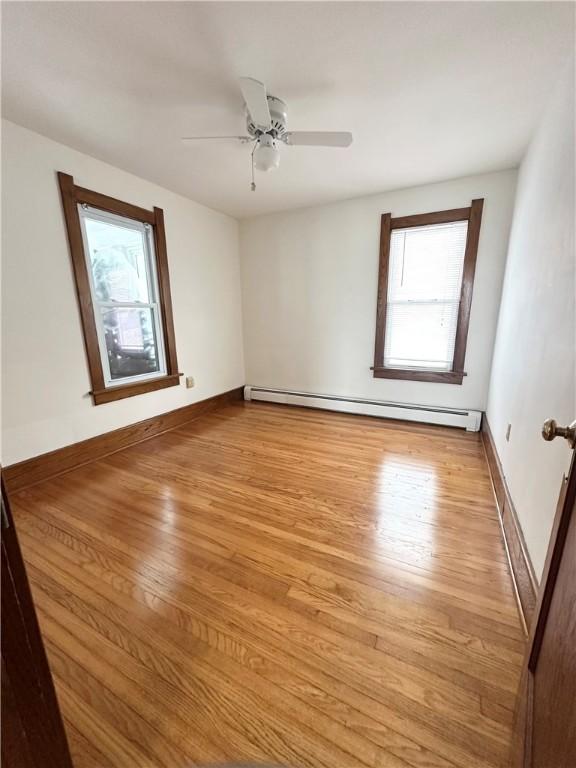 empty room with a baseboard heating unit, light wood finished floors, baseboards, and a ceiling fan
