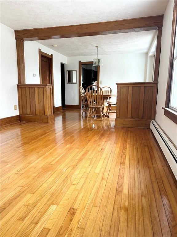 dining area featuring beamed ceiling, light wood-style floors, baseboard heating, a chandelier, and baseboards