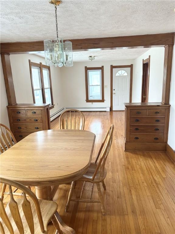 dining area with a chandelier, a textured ceiling, baseboard heating, light wood-style floors, and beamed ceiling