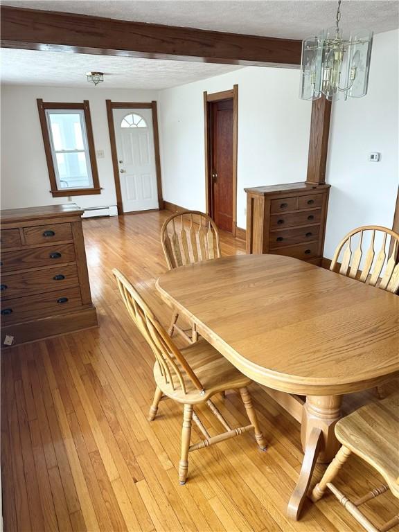 dining area featuring hardwood / wood-style floors, a chandelier, beam ceiling, a baseboard heating unit, and baseboards