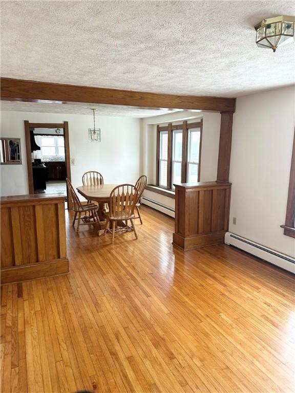 dining space with light wood-style flooring, a baseboard radiator, a textured ceiling, and beam ceiling