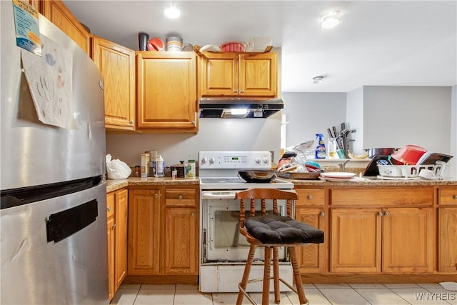 kitchen with freestanding refrigerator, white electric range oven, under cabinet range hood, light tile patterned flooring, and brown cabinets