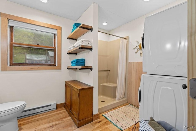 full bath featuring baseboard heating, stacked washing machine and dryer, a stall shower, wood finished floors, and toilet