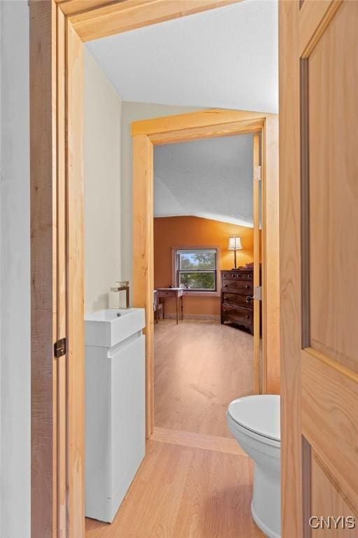 half bath with toilet, vaulted ceiling, and wood finished floors