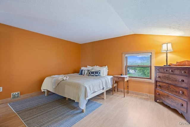 bedroom with light wood-type flooring, vaulted ceiling, baseboards, and a textured ceiling