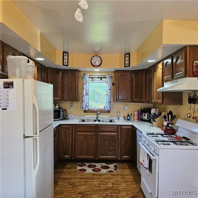 kitchen featuring white appliances, a sink, under cabinet range hood, light countertops, and dark wood-style flooring