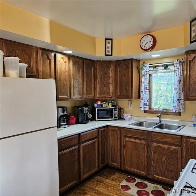 kitchen with freestanding refrigerator, a sink, stainless steel microwave, light countertops, and dark wood-type flooring