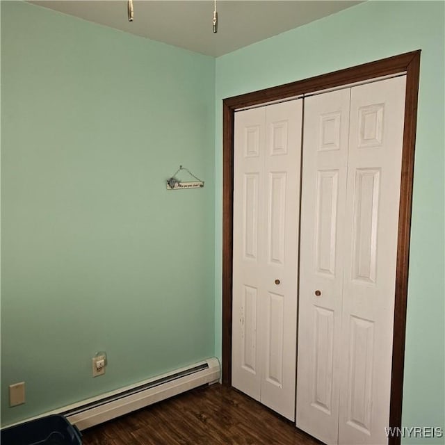 unfurnished bedroom featuring a baseboard radiator, a closet, and dark wood-type flooring