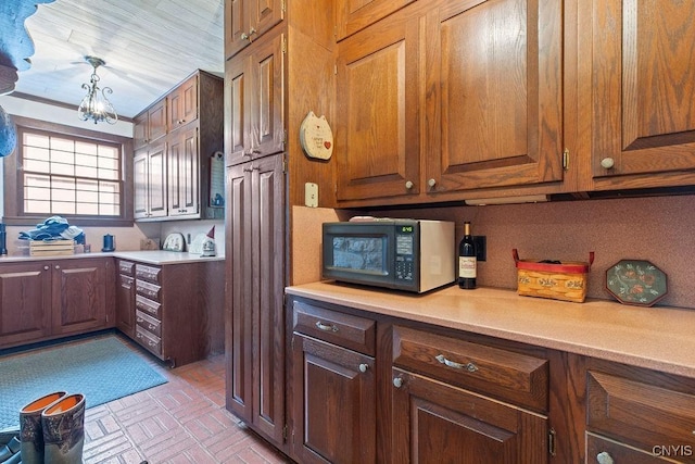 2066 Deerlick Rd, Cape Vincent, NY 13618 - kitchen featuring black microwave, light countertops, brick patterned floors, a chandelier, and brown cabinetry