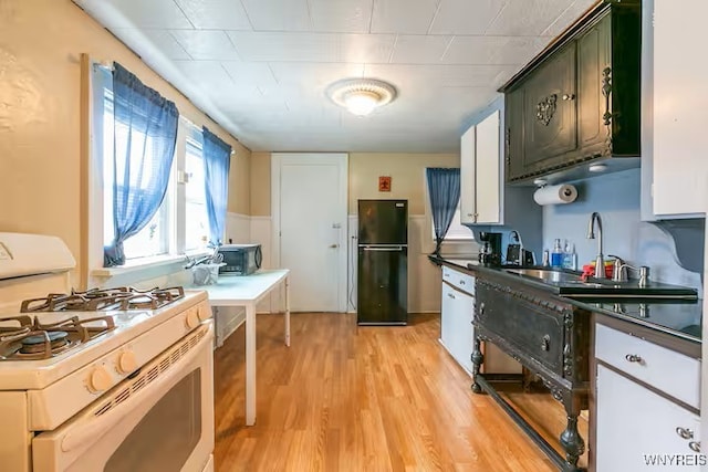 kitchen featuring white range with gas cooktop, freestanding refrigerator, light wood-style flooring, and dark countertops