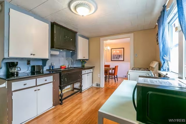 kitchen featuring white cabinetry, dark countertops, light wood-style floors, white gas stove, and a sink