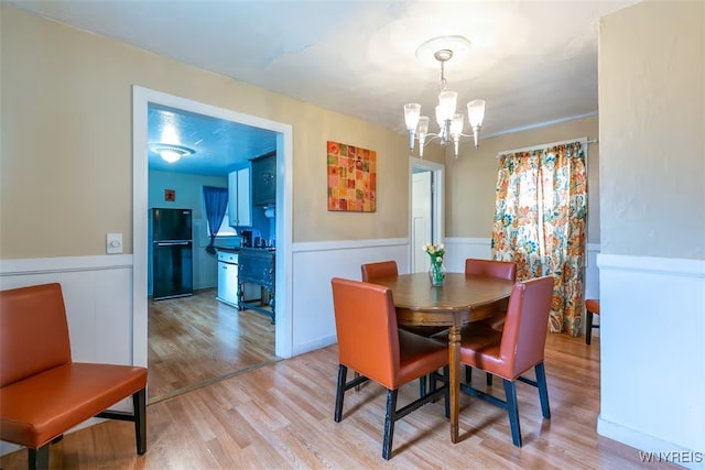 dining space with a chandelier, light wood finished floors, and a wainscoted wall