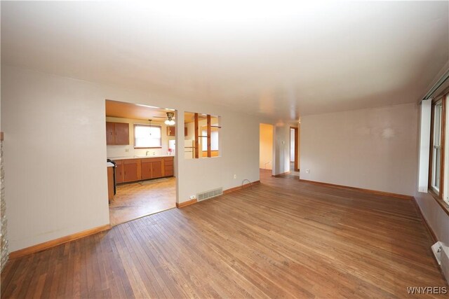 unfurnished living room with light wood finished floors, baseboards, a ceiling fan, and a sink