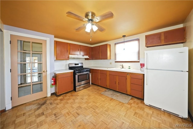 kitchen with freestanding refrigerator, stainless steel gas range, under cabinet range hood, light countertops, and a sink