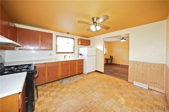 kitchen featuring freestanding refrigerator, stainless steel gas stove, light countertops, a ceiling fan, and under cabinet range hood
