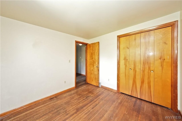 unfurnished bedroom featuring hardwood / wood-style floors, baseboards, and a closet
