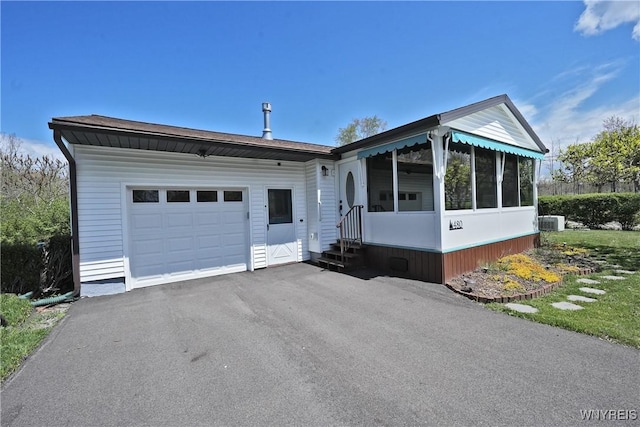view of front of property featuring driveway, a garage, a sunroom, and cooling unit