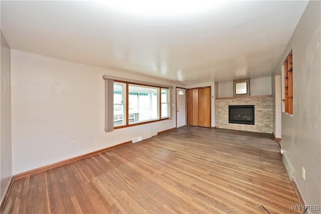 unfurnished living room featuring light wood finished floors, a glass covered fireplace, and baseboards