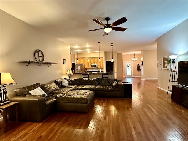living area featuring dark wood-style flooring, a ceiling fan, a chandelier, and baseboards