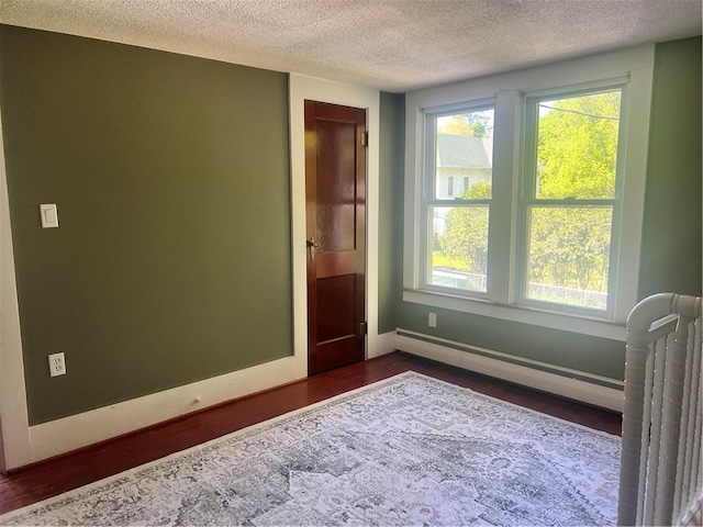 unfurnished room featuring baseboard heating, a textured ceiling, dark wood-style floors, and baseboards