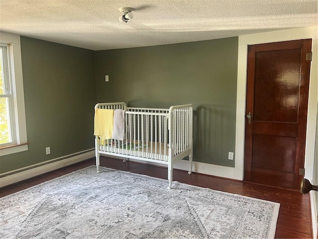 bedroom with wood finished floors, a textured ceiling, baseboards, and a baseboard radiator