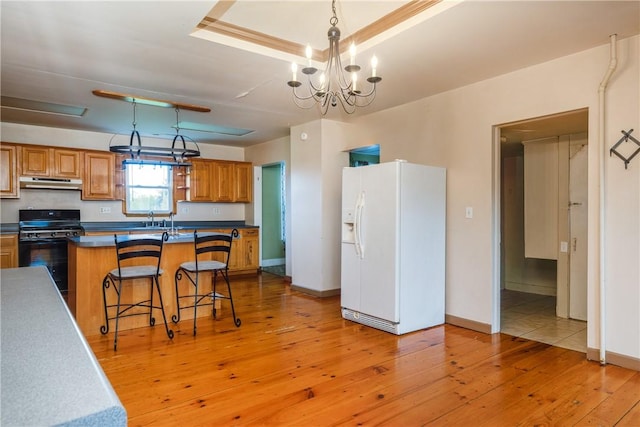 448 Old Ithaca Rd, Horseheads, NY 14845 - kitchen featuring white fridge with ice dispenser, black gas stove, brown cabinetry, under cabinet range hood, and a chandelier