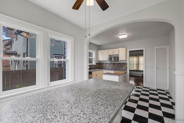 kitchen with arched walkways, appliances with stainless steel finishes, dark floors, a ceiling fan, and a sink