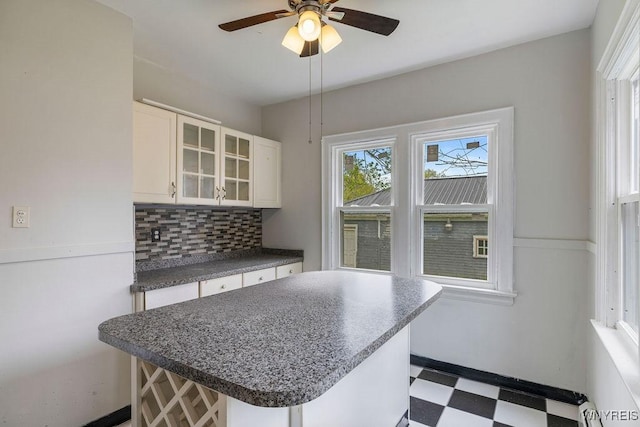 kitchen featuring tile patterned floors, dark countertops, tasteful backsplash, glass insert cabinets, and ceiling fan