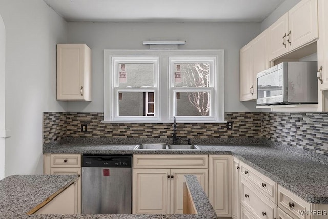 kitchen with stainless steel dishwasher, a sink, backsplash, and cream cabinets