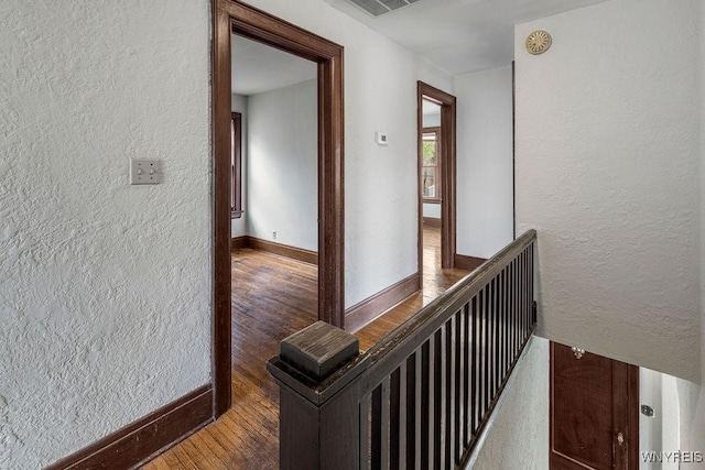 hall with hardwood / wood-style floors, a textured wall, and baseboards