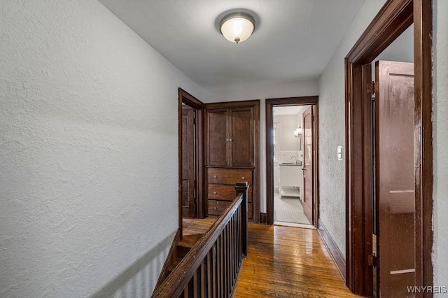 corridor featuring a textured wall, dark wood-style flooring, baseboards, and a sink