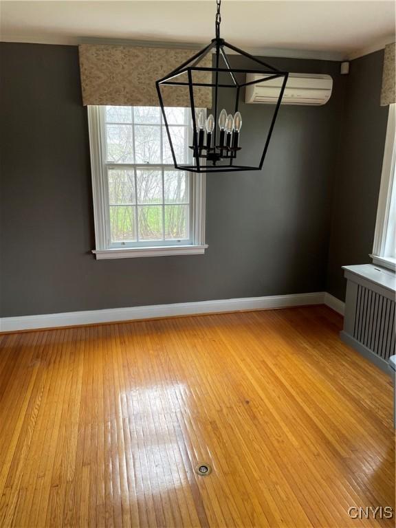 10 Sage Ct, Utica, NY 13502 - unfurnished dining area featuring a wall mounted AC, baseboards, hardwood / wood-style flooring, radiator heating unit, and a chandelier