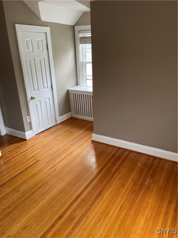 10 Sage Ct, Utica, NY 13502 - additional living space featuring baseboards, vaulted ceiling, light wood-type flooring, and radiator heating unit
