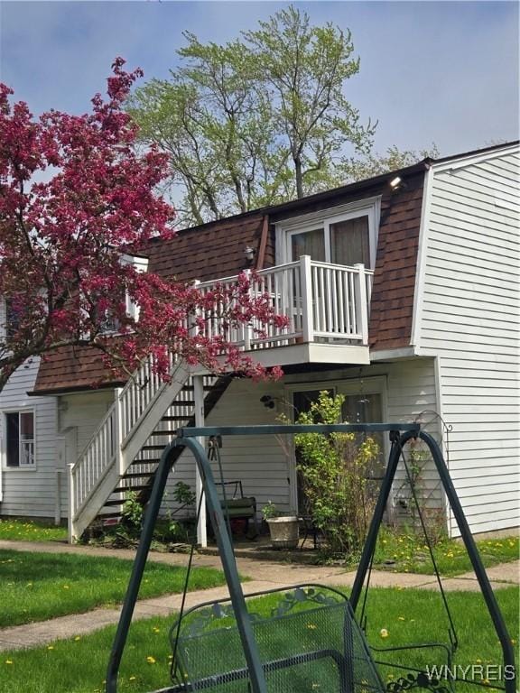 rear view of house featuring roof with shingles, a lawn, a gambrel roof, and stairs