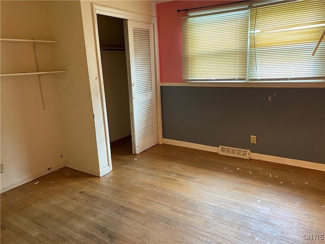 unfurnished bedroom with wood-type flooring, a closet, and baseboards