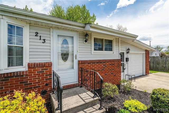 doorway to property featuring brick siding, driveway, a garage, and fence