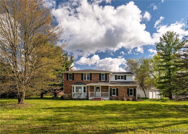 view of front facade with a front yard, a porch, a chimney, and brick siding