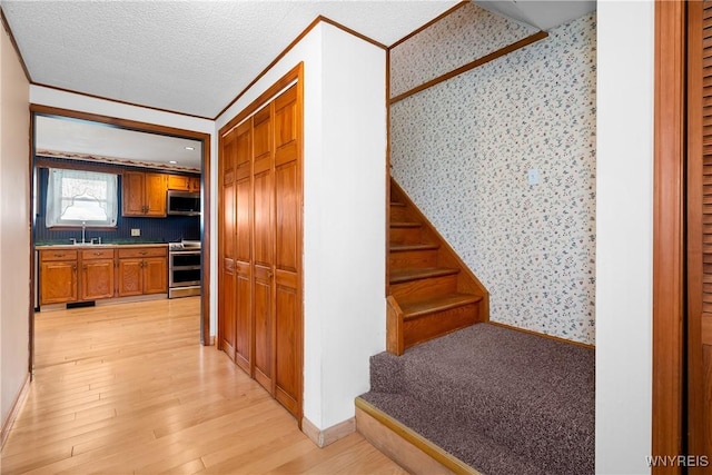 stairway featuring wallpapered walls, wood finished floors, baseboards, and crown molding