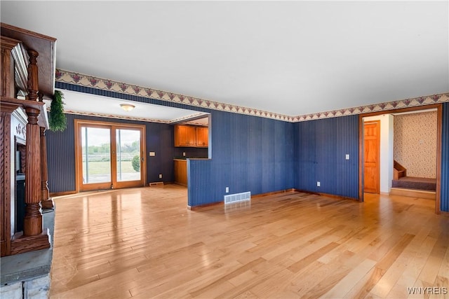 unfurnished living room with light wood-style flooring, wallpapered walls, stairway, and baseboards