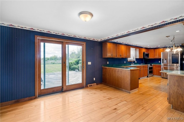 kitchen featuring appliances with stainless steel finishes, wallpapered walls, a peninsula, brown cabinetry, and a sink