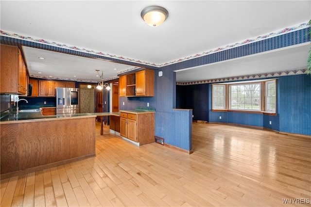 kitchen featuring stainless steel fridge with ice dispenser, wallpapered walls, a sink, open shelves, and brown cabinetry