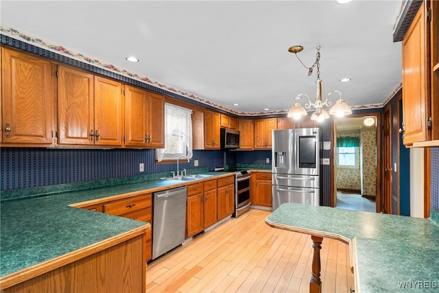 kitchen featuring stainless steel appliances, a sink, wallpapered walls, plenty of natural light, and brown cabinetry