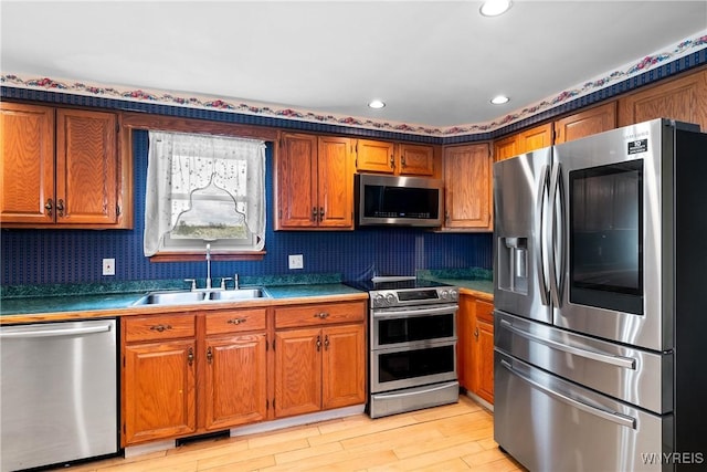 kitchen with appliances with stainless steel finishes, a sink, brown cabinetry, light wood-type flooring, and recessed lighting
