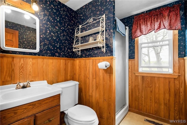 bathroom with wainscoting, wallpapered walls, a stall shower, vanity, and toilet