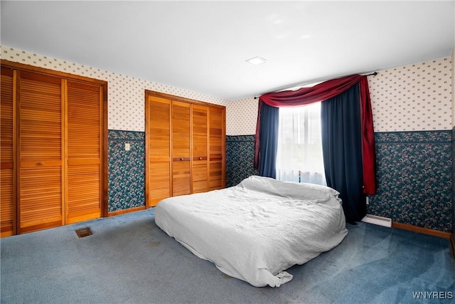 bedroom featuring wallpapered walls, multiple closets, a baseboard heating unit, carpet, and baseboards