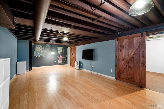 finished below grade area featuring a barn door, wood finished floors, and baseboards
