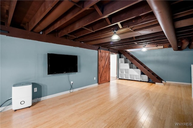 finished below grade area with a barn door, wood finished floors, baseboards, and stairway