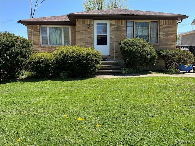 view of front facade featuring brick siding, a front yard, and roof with shingles